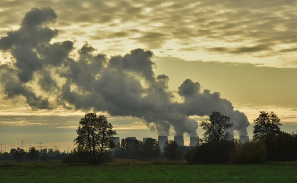 Smoke and emissions rising from an industrial power station beneath a cloudy sky