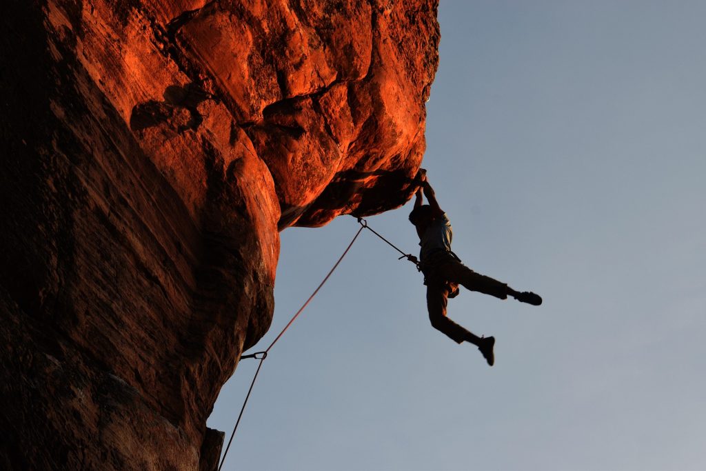 Rock climber ascending a dramatic sandstone cliff during sunset with safety ropes